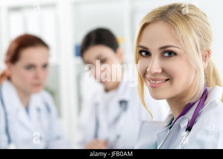 Porträt des Lächelns weibliche Medizin Arzt mit zwei Kollegen, die im Hintergrund arbeiten. Gesundheitswesen und Medizin-Konzept. Stockfoto