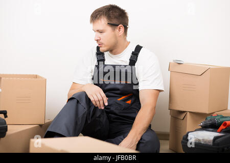 Frustriert Mann sitzt zwischen braunen Kartons nach dem Umzug nicht zu wissen, was zu tun ist. DIY, neue Heimat und bewegende Konzept Stockfoto