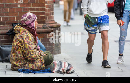 Obdachlose Dame sitzt auf dem Boden wie Menschen ignorieren sie vorbeigehen. Stockfoto