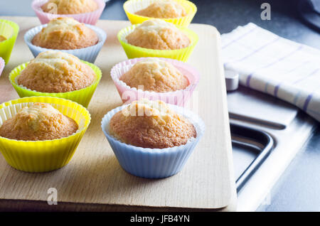 Küche-Szene mit Reihen von frisch gebackenen Muffins in bunten Backen Fällen auf Holzbrett ruht auf Herd Kochfeld.  Ein aufgegebenes Teatowel und Arbeitsplatte ar Stockfoto