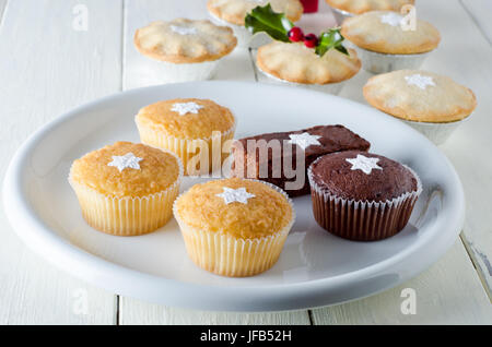 Weihnachten Kuchen auf einem Teller mit Stars aus gesiebten Puderzucker mit Mince Pies und Holly in soft-Fokus Hintergrund dekoriert. Ausgebreitet auf einem weißen, planen Stockfoto