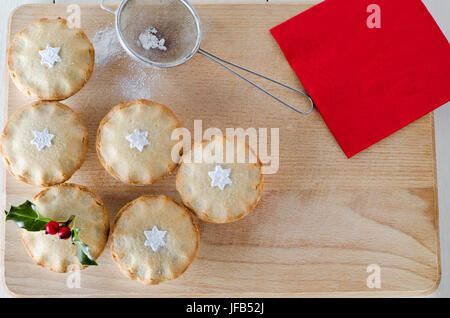 Overhead Schuss von Mince Pies mit Holly Zweig eingerichtet und gesiebt Puderzucker in Sternformen.  Ein Alter Tee Sieb pressen sitzt auf Holzbrett mit sp Stockfoto