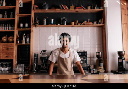 Porträt von professionellen Barista am Café Zähler stehen. Afrikanischer Mann in Schürze Blick in die Kamera und lächelnd. Stockfoto