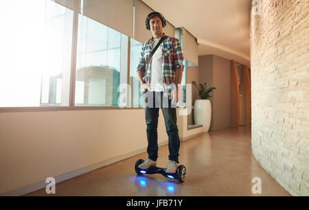 Voller Länge Schuss stilvollen jungen Mannes Reiten auf elektrische selbstbalancierende Scooter im modernen Büro-Korridor. Stockfoto