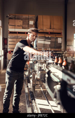 Brewer, die Aufsicht über den Prozess der Bierherstellung in der Brauerei. Junger Mann am Bier Abfüllanlage in Betrieb. Stockfoto