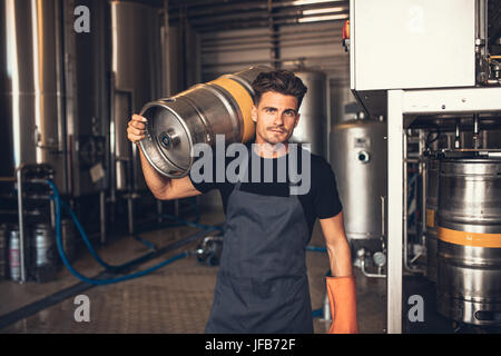 Porträt von männlichen Brewer Metallbehälter werkseitig Brauerei tragen. Junger Mann hält ein Fass auf Schulter am Lager. Stockfoto