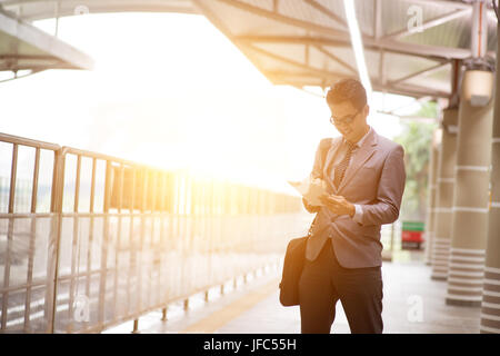 Asiatische Geschäftsmann mit digitalen TabletPC bei Metro Transit-Plattform, mit schönen Sonne Streulicht im Hintergrund. Stockfoto