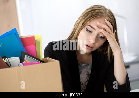 Junge entlassen Arbeitnehmerin sitzt neben dem Karton mit ihren Habseligkeiten im Büro nicht zu wissen, was als nächstes zu tun. Gebrannten Konzept bekommen. Stockfoto