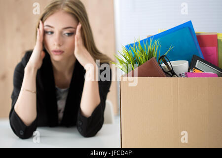 Junge entlassen Arbeitnehmerin sitzt neben dem Karton mit ihren Habseligkeiten im Büro nicht zu wissen, was als nächstes zu tun. Gebrannten Konzept bekommen. Stockfoto