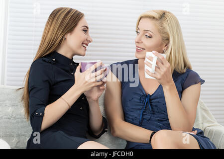 Zwei Freundinnen reden und Lachen gemeinsam auf Sofa sitzen, während der Kaffeepause. Stockfoto