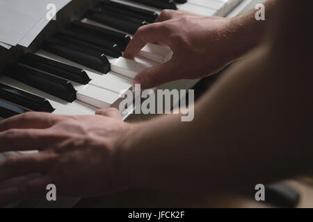 Nahaufnahme von Mann Klavier zu spielen. Intimer Blick auf Hände auf Tasten der Tastatur. Filmische und dramatische Atmosphäre und Ambiente-Beleuchtung. Talentierter Pianist. Stockfoto