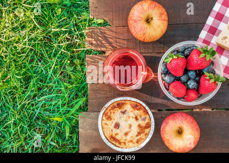 Eine obenliegende Foto eines Picknicks mit einen Apfel, ein Glas rose Wein, frisches Obst in einem Plastikbehälter und eine Quiche auf einem rustikalen Holzbrett auf Top o Stockfoto