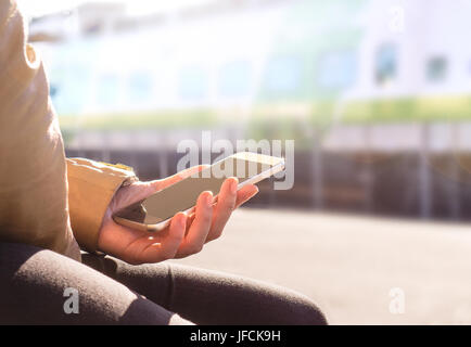 Frau-Ticket kaufen oder überprüfen Fahrplan mit dem Handy in den Bahnsteig. Smartphone und TrainModern ÖPNV-Konzept. Stockfoto