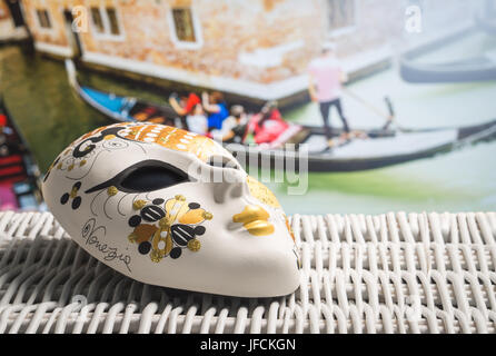Authentische Maske aus Venedig mit einem Gondoliere und Touristen in der Gondel im Hintergrund. Goldene Souvenirs und traditionellen venezianischen Boot im Kanal. Stockfoto