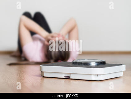 Gewicht-Verlust-Fail-Konzept. Skala und deprimiert, frustriert und traurig Frau Stock hält Kopf und Arme auf Knien sitzen. Stockfoto