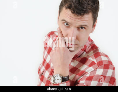 Ernsten jungen Mann in Hipster Shirt hält Hand am Kinn und vor weißem Hintergrund stehen. Emotionales Konzept Stockfoto