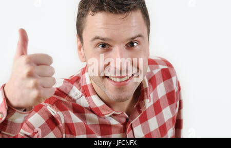 Lächelnd jungen Mann in Hipster-Shirt zeigt Daumen oben und stehen vor weißem Hintergrund. Emotionales Konzept Stockfoto