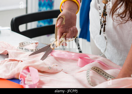 Nahaufnahme der weiblichen Kleidung Maker Hände schneiden etwas. Schneiderin arbeitet in ihrem Atelier. Handgefertigte Kleidung Stockfoto