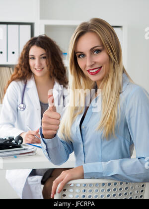 Weibliche Patienten zeigt "OK" Zeichen mit Daumen im Arztzimmer sitzt lächelnd. Hohes Niveau und Qualität medizinischer Service-Konzept. Beste Behandlung und pati Stockfoto