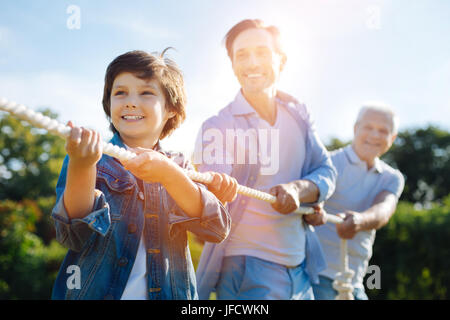 Echte Unterstützung. Begeisterte konzentrierte schöne Familie handeln als Team während des Spielens zu zerren, Krieg und Spaß im Freien im park Stockfoto