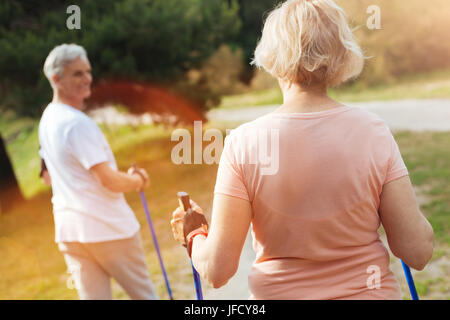Outdoor-Übungen. Sportlich gut gebaut Seniorin üben, Nordic walking und mit Blick auf ihren Mann während der Bewegung in der Natur Stockfoto