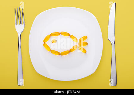 Fisch Öl weiche Gele liegen auf weißem Porzellanteller in Form von Fisch (gelb hinterlegt) Stockfoto