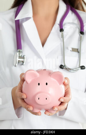 Frau Doktor Holding Sparschwein. Des Arztes Hände Nahaufnahme. Medizinische Versicherung und Gesundheitswesen Konzept. Stockfoto