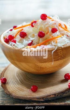 Mit Preiselbeeren und Karotten in eine hölzerne Schüssel Sauerkraut. Stockfoto