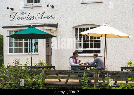 Zwei junge Männer, die im Juni vor dem Dundas Arms Pub in Kintbury, West Berkshire, Großbritannien, etwas zu essen und zu trinken haben Stockfoto