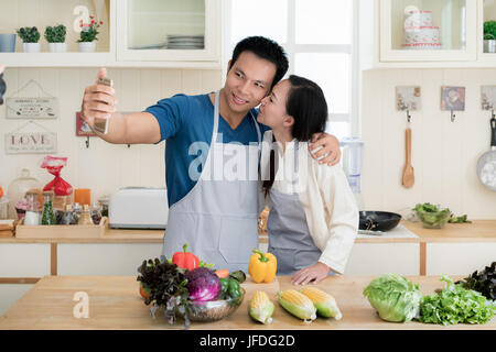 Asiatische gut aussehend Mann lächelt und kochen in der Küche dabei Selfie mit Smartphone zu Hause. Glückliche Liebe paar Konzept. Stockfoto