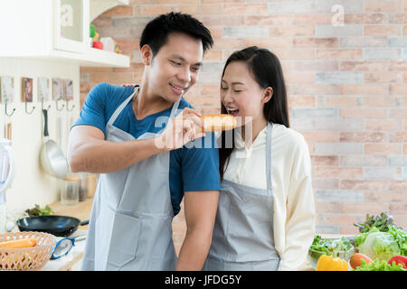 Asiatischen schöne junge Paar füttert Brot Lächeln beim Kochen in der Küche zu Hause. Glückliche Liebespaar im Haus. Stockfoto