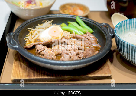 Koreanische gegrilltes Schweinefleisch in heißer Pfanne mit Ei, sprießen und Erbsen auf Seite. Stockfoto