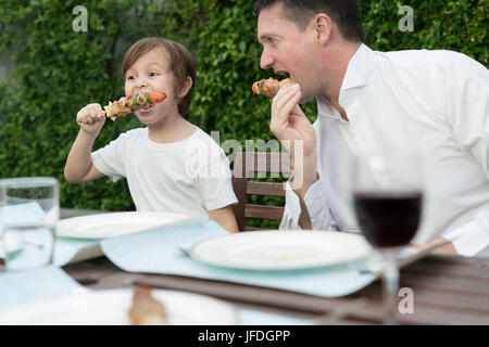 Vater mit kleinen Bcute jungen Grill in Familie Mittagessen Zeit zu Hause zu essen. Stockfoto