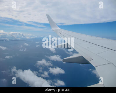 Blick auf die Tragfläche eines Flugzeugs entnommen innen durch das Fenster. Zeigt einen schönen blauen Himmel mit Wolken. Stockfoto