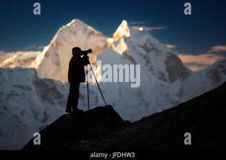 Eine Silhouette eines Mannes (Fotograf) stehend auf einem Hügel vor den Bergen. Stockfoto