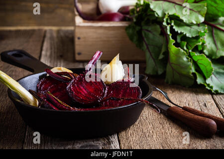 Geröstete rote Beete in gusseisernen Pfanne und frischem Gemüse in Kiste auf rustikalen Holztisch Stockfoto