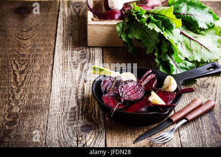 Geröstete rote Beete in gusseisernen Pfanne und frischem Gemüse in Kiste auf rustikalen Holztisch Stockfoto