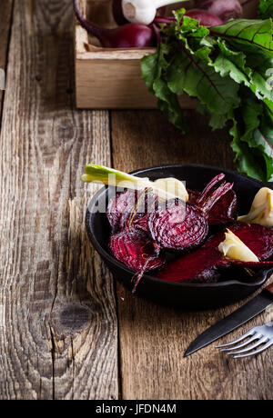 Geröstete rote Beete in gusseisernen Pfanne und frischem Gemüse in Kiste auf rustikalen Holztisch Stockfoto