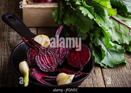 Geröstete rote Beete in gusseisernen Pfanne und frischem Gemüse in Kiste auf rustikalen Holztisch Stockfoto