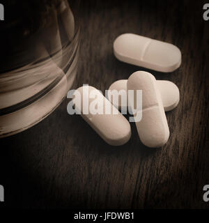 Tabletten und ein Glas Wasser auf einen Tisch Stockfoto