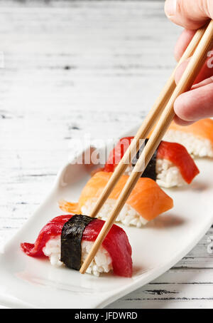 Satz von Lachs und roten Thunfisch Nigiris auf weißen Teller über alte weiße Holz mit Stäbchen. Roher Fisch in traditionelles japanisches Sushi-Stil. Vertikales Bild. Stockfoto