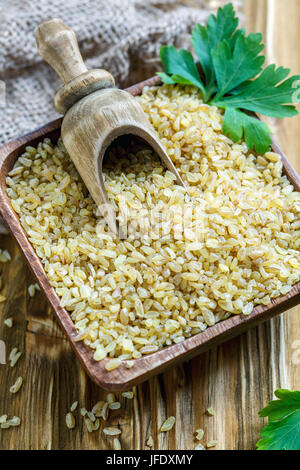 Bulgur und hölzerne Schaufel in eine Schüssel geben. Stockfoto