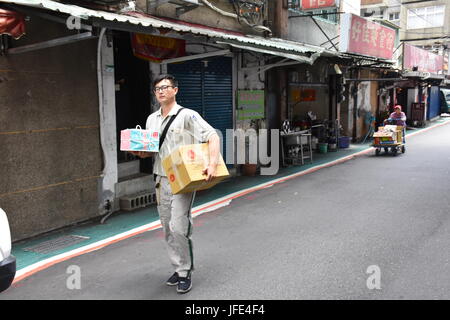 Hart arbeitender Lieferung Typ holt Pakete mit alten Person Recycling Wagen schieben, um Geld zu verdienen an anderer Stelle im 94F Wetter ausgeliefert werden. Stockfoto
