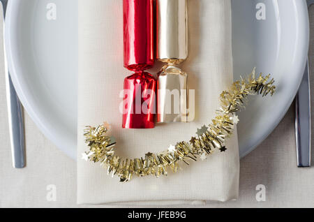 Overhead Schuss, Weihnachtsessen, mit roten und goldenen Cracker und Lametta gelegt auf einer Serviette, Teller, Besteck und Tischdecken unter darstellt. Stockfoto