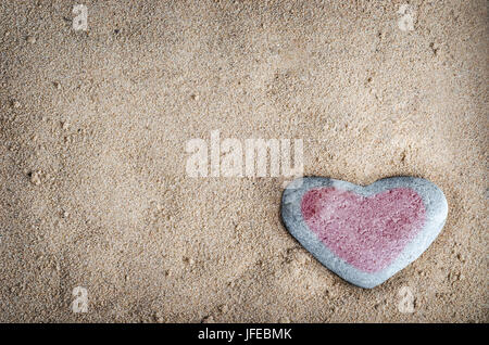 Eine graue herzförmige Stein auf körnigen Sand, getönt mit einem roten Herzen.  Diese Version ist vignetted und bearbeitet, um ein Retro oder lo-Fi aussehen zu verleihen. Stockfoto