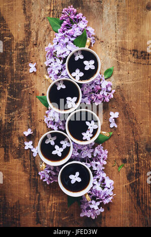 Stillleben-Komposition mit lila Blüten und Tassen schwarzen Kaffee am rustikalen Holztisch. Ansicht von oben Stockfoto