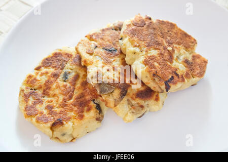 Kartoffelkuchen mit Pilzen auf einem weißen Teller. Kartoffelpuffer, ein Snack auf pflanzlicher Basis. Stockfoto