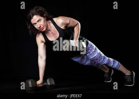 Intensives Bild eines weiblichen Gewichthebers am schwarzen Brett Dumbell Folge zu tun. Stockfoto