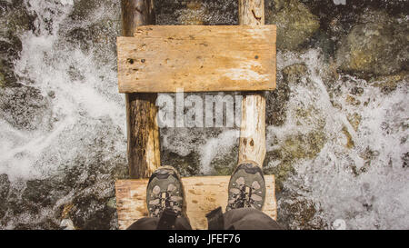 Stiefel auf einer Holzbrücke über einen schnellen Bach Stockfoto