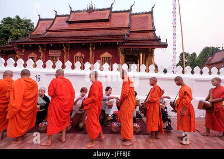 Buddhistische Mönche tragen orangefarbene Gewänder Spaziergang durch den Tempel Wat Sensoukaram Geschenke auf den Straßen von Luang Prabang, Laos, Asien zu sammeln Stockfoto